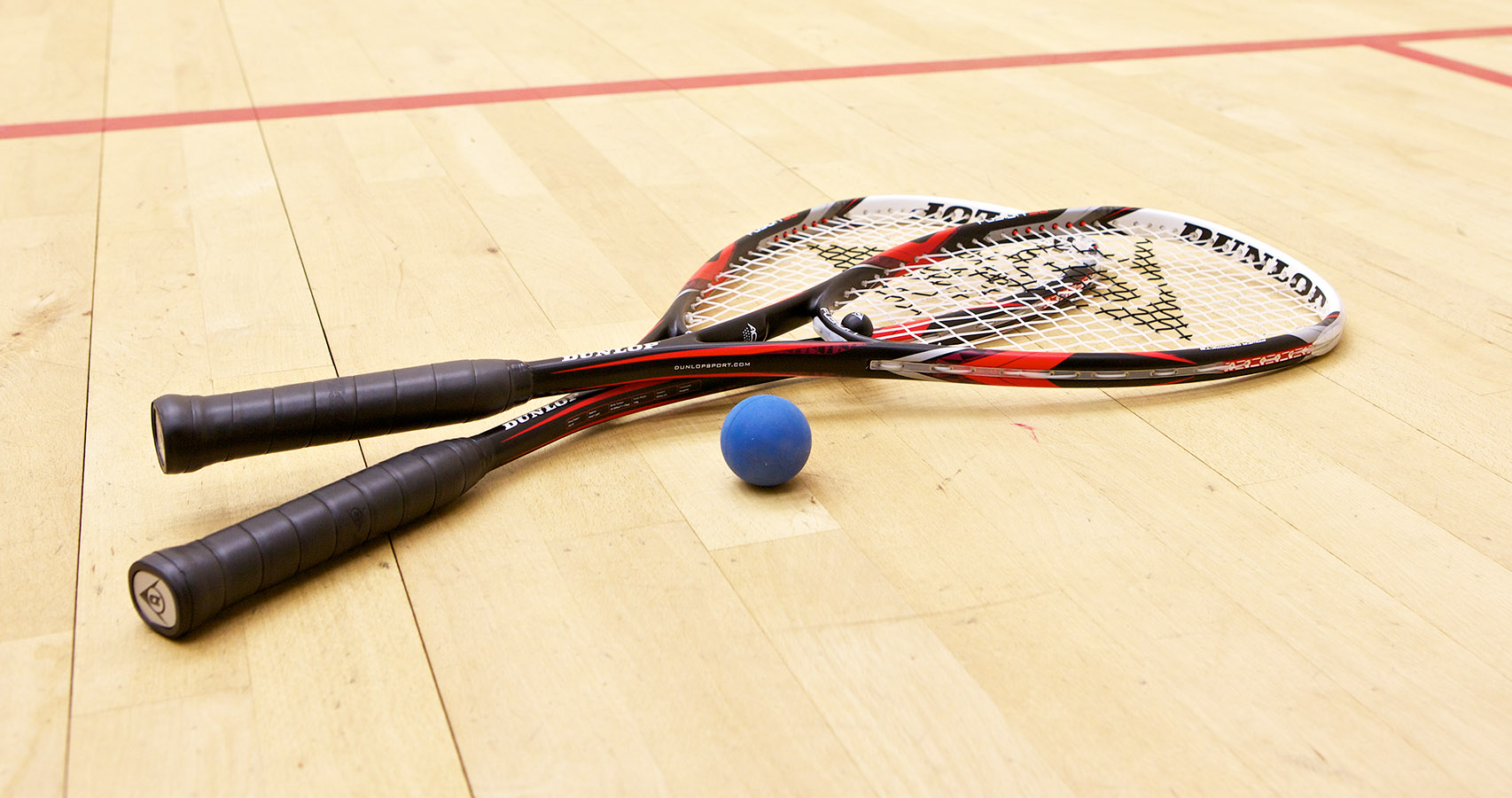 Two squash rackets and a ball rest on a court floor.
